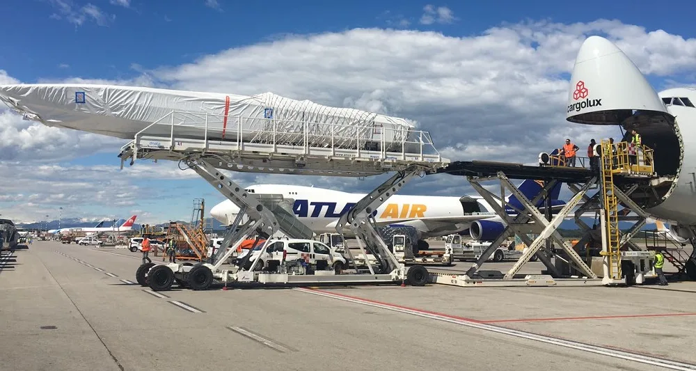 Shrink-wrapped boat raised on a high loader beside the open nose of a Boeing 747 freighter