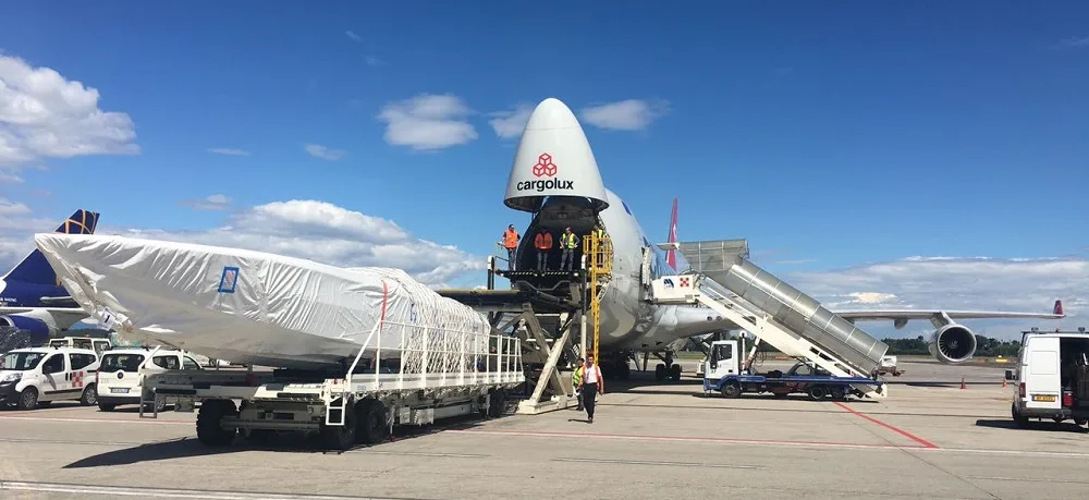 Shrink-wrapped boat on a transporter on the airport apron next to a 747 freighter