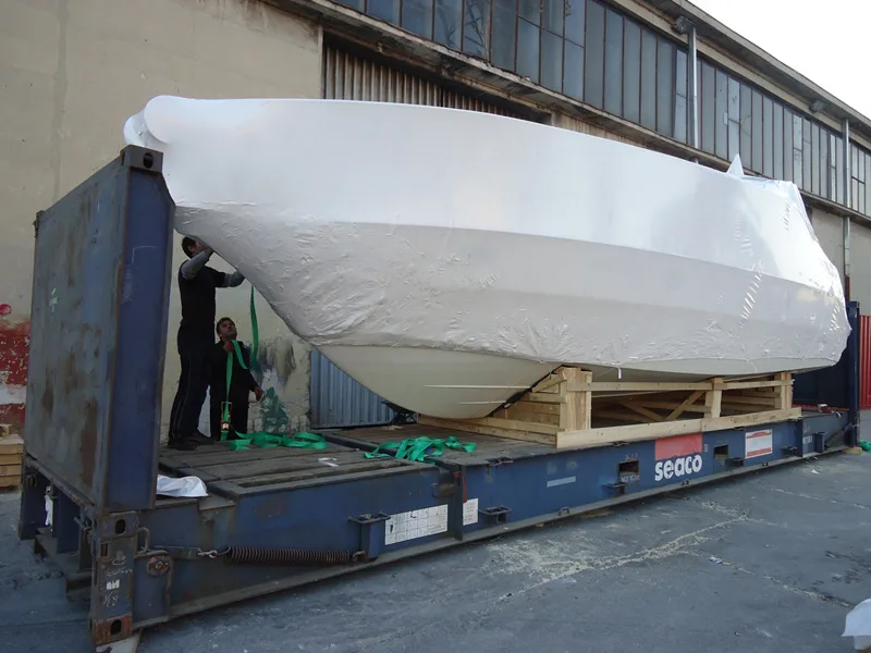 Shrink-wrapped motor boat on timber supports on a flat rack container