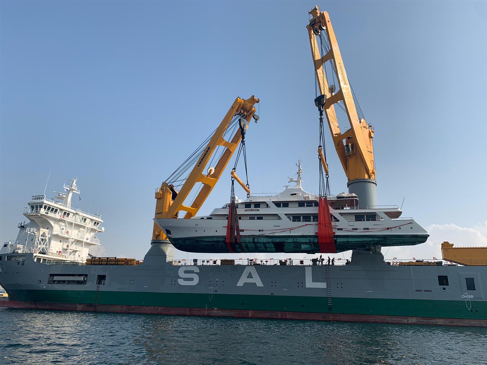Superyacht lifted by the cranes of a heavy lift ship for transport to Singapore
