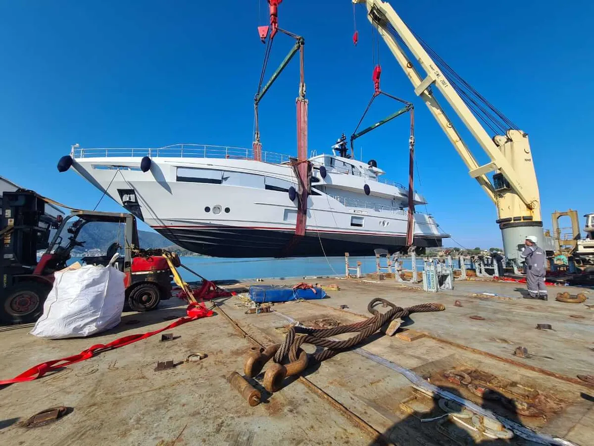 Motor yacht lifted in slings hung from spreader bars by the ship's cranes
