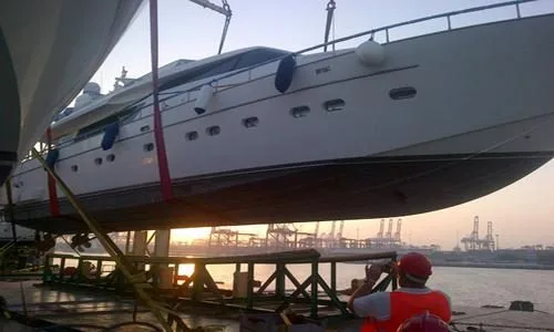 Motor yacht lifted by a ship's crane at dusk during loading
