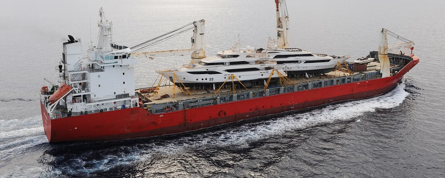 Cargo ship at sea carrying two superyachts on deck