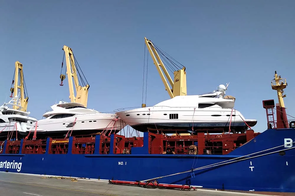Motor yachts standing on cradles on the deck of a heavy lift ship alongside the quay
